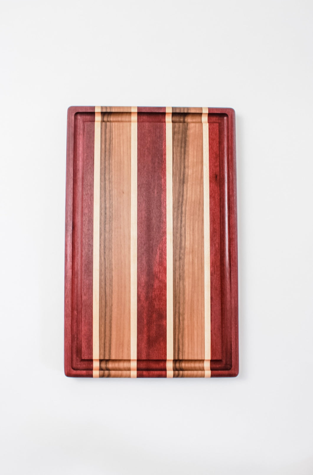 Handmade cutting board with strips of purpleheart, walnut and maple wood featuring a juice groove.