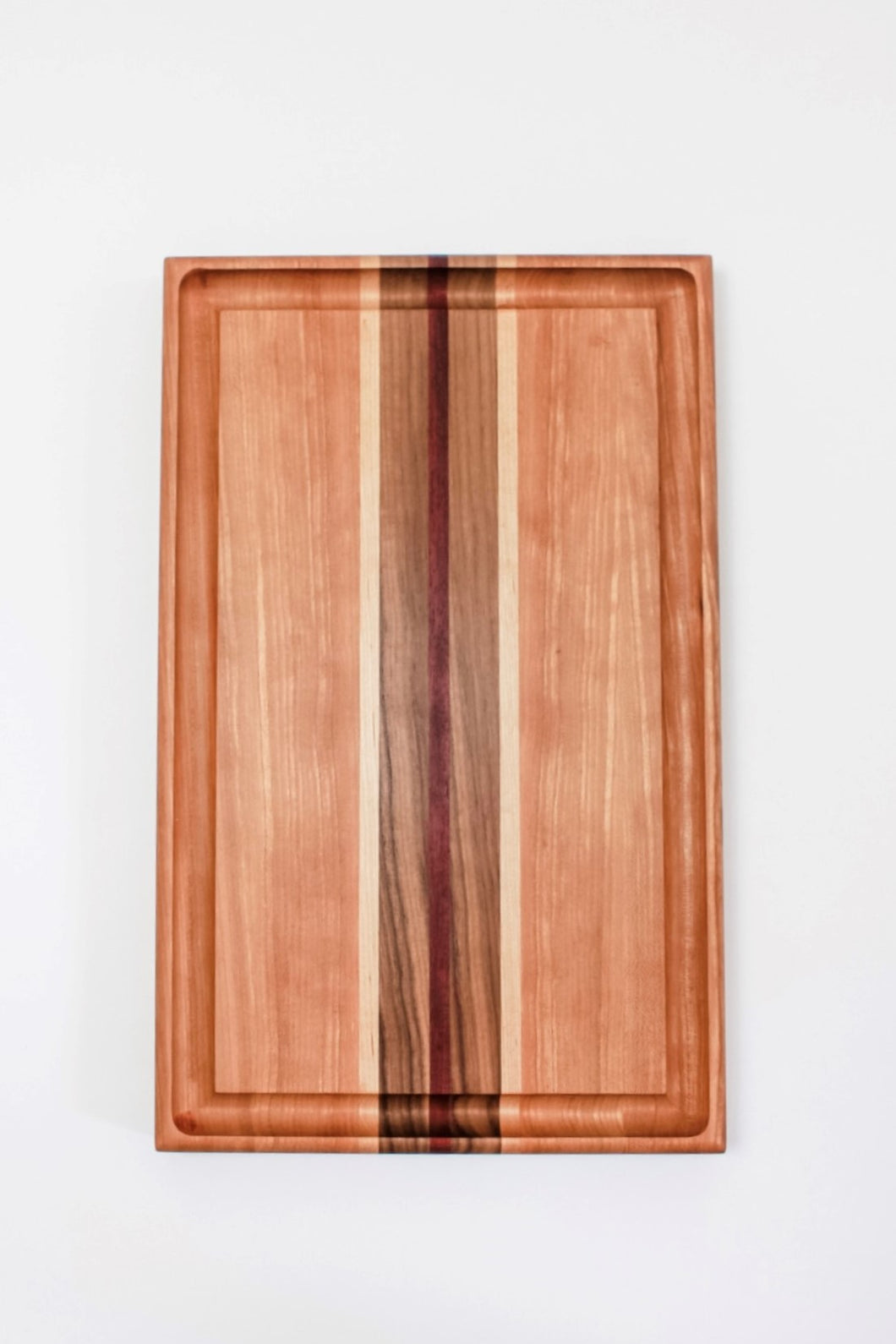 Cutting board made with cherry wood and strips of purpleheart, walnut and maple wood. This board features a juice groove.